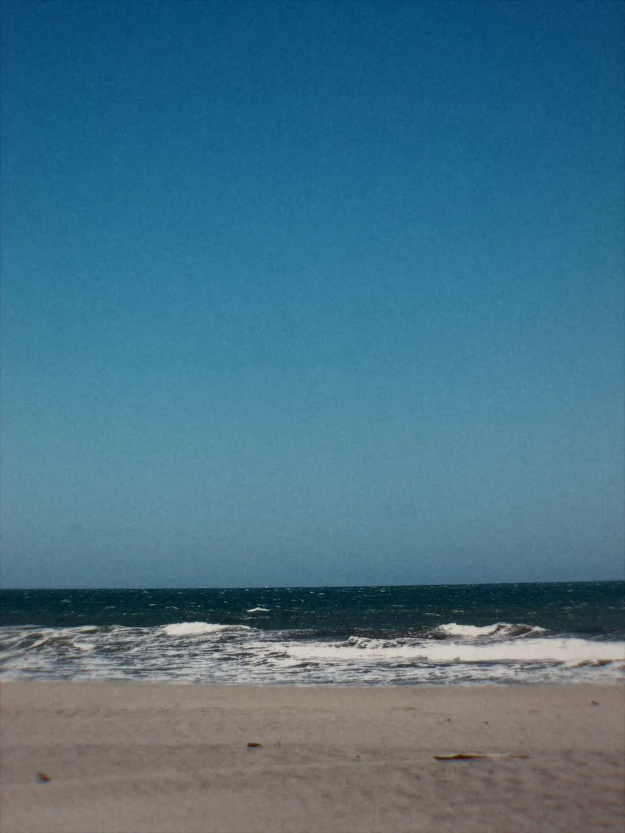 Surf running up an empty beach under a deep blue sky