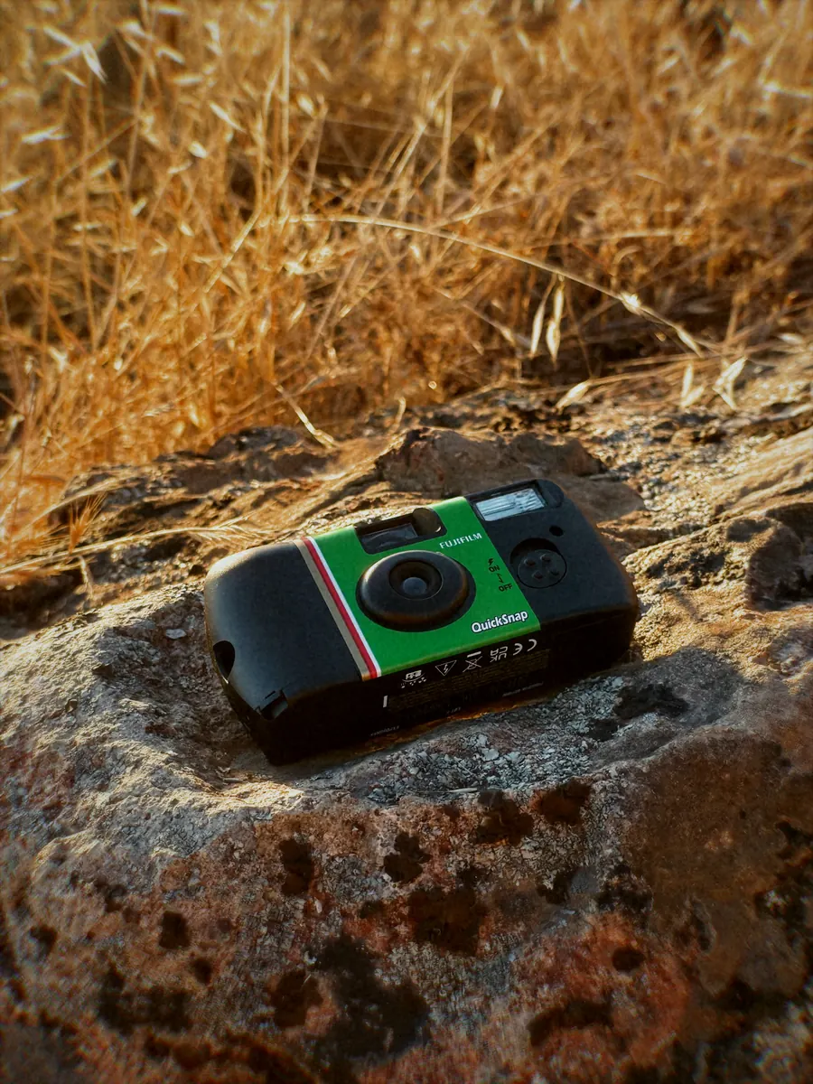 A Fujifilm QuickSnap disposable camera resting on a rock in dry grass